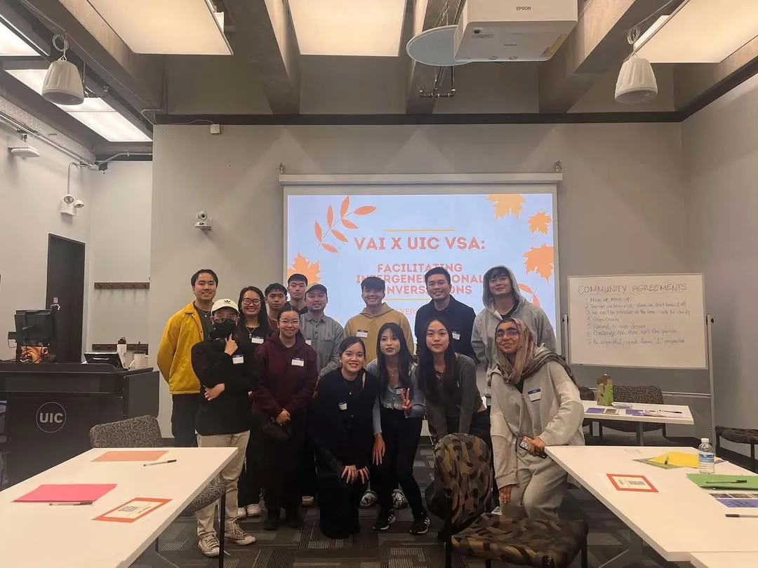 A group of workshop participants in a classroom in front of a projected slide reading “VAI X UIC VSA: Facilitating Intergenerational Conversations”.